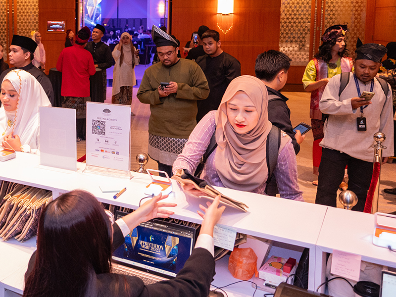 Busy event registration desk with check-in crew assisting attendees collecting their credentials at a Malaysian corporate event